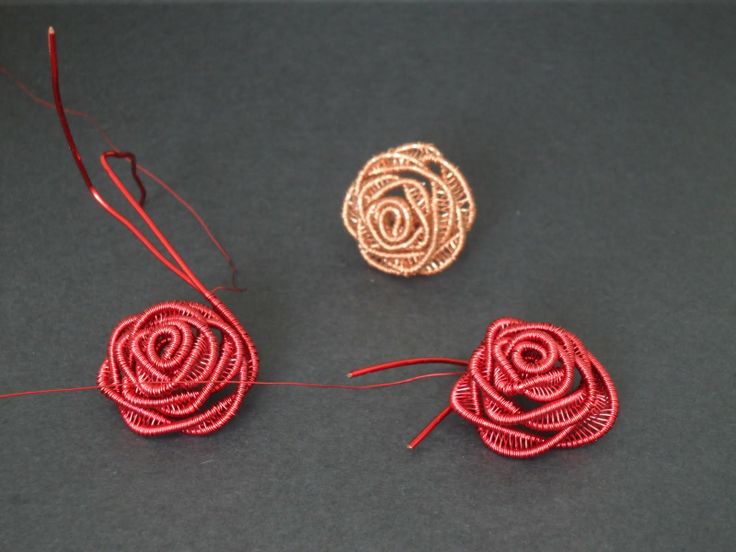 three pieces of red thread sitting next to each other on a black surface with two small rose shaped pins