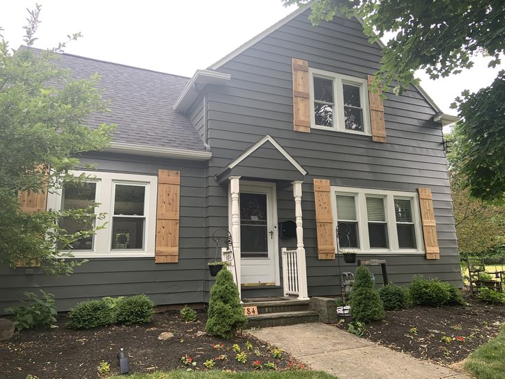 a gray house with wooden shutters on the front door and side windows is shown