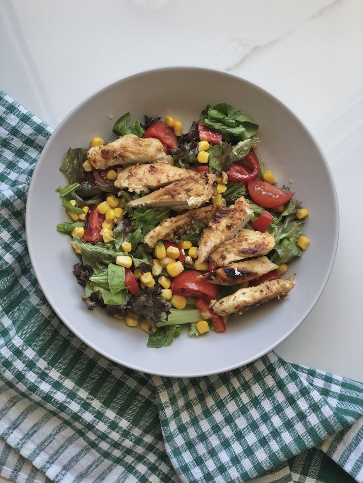 a white bowl filled with chicken and veggies on top of a green checkered napkin