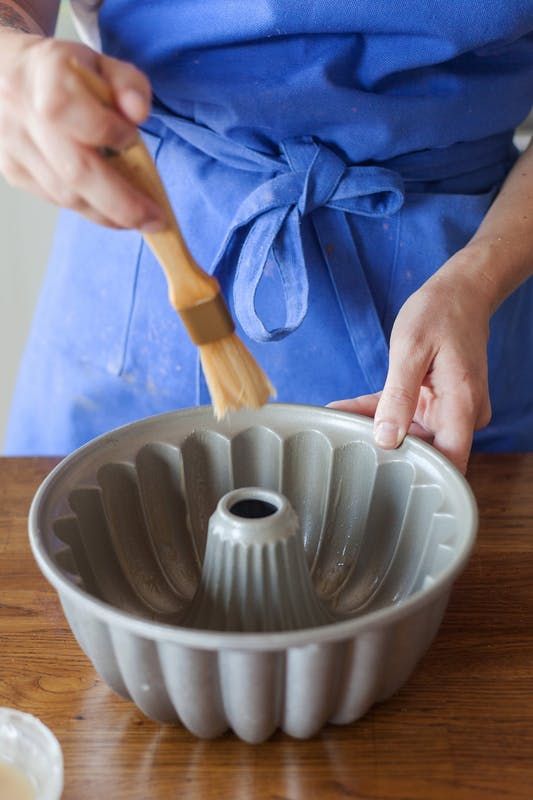 a person in an apron using a spatula to mix batter into a bundt cake