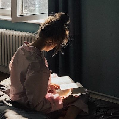 a woman sitting on the floor reading a book in front of a radiator