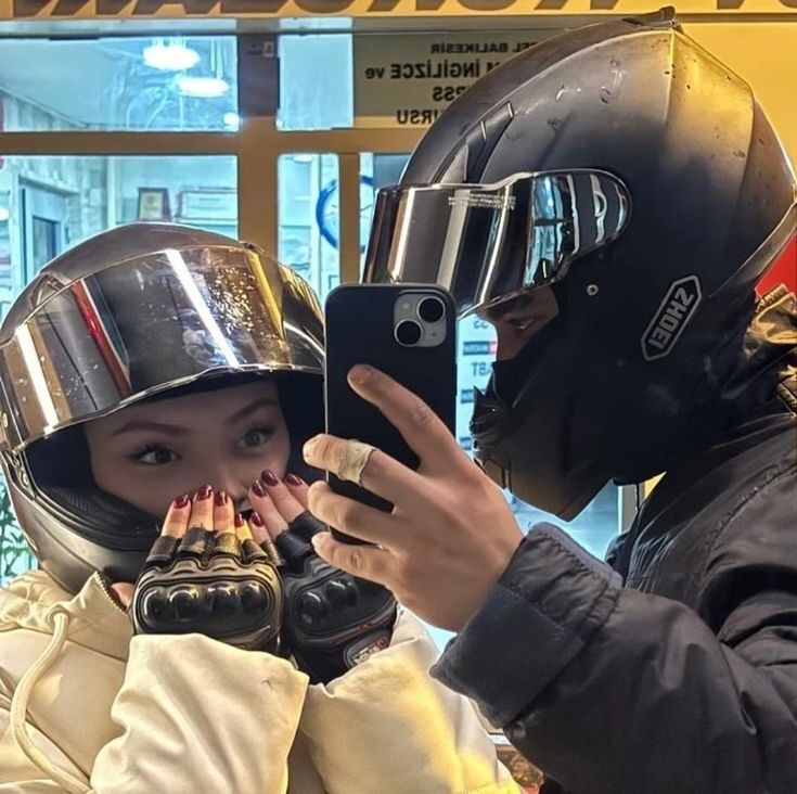 two people wearing helmets taking pictures with their cell phones