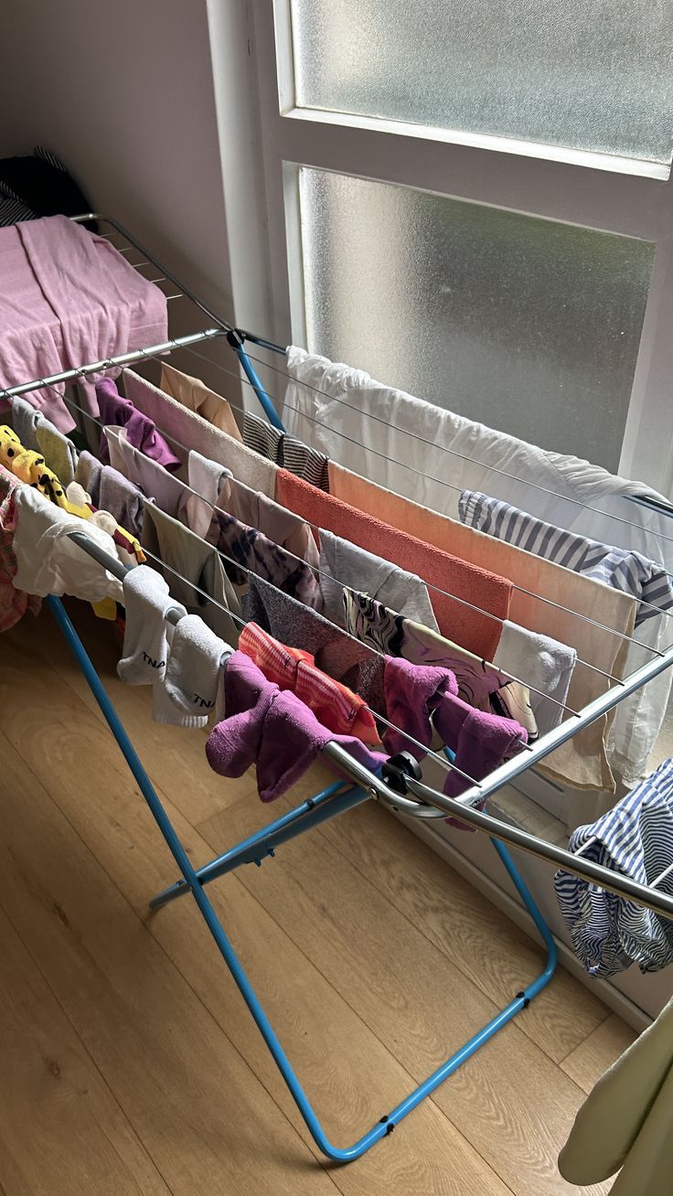 an ironing board with clothes hanging from it's sides in front of a window