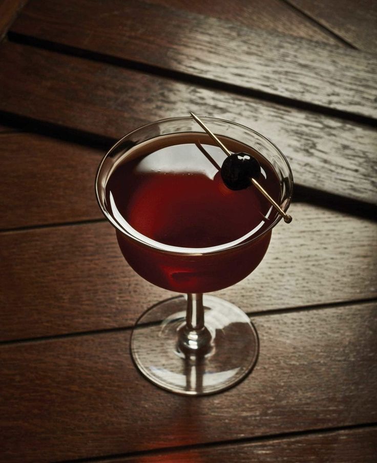 a glass filled with red liquid on top of a wooden table