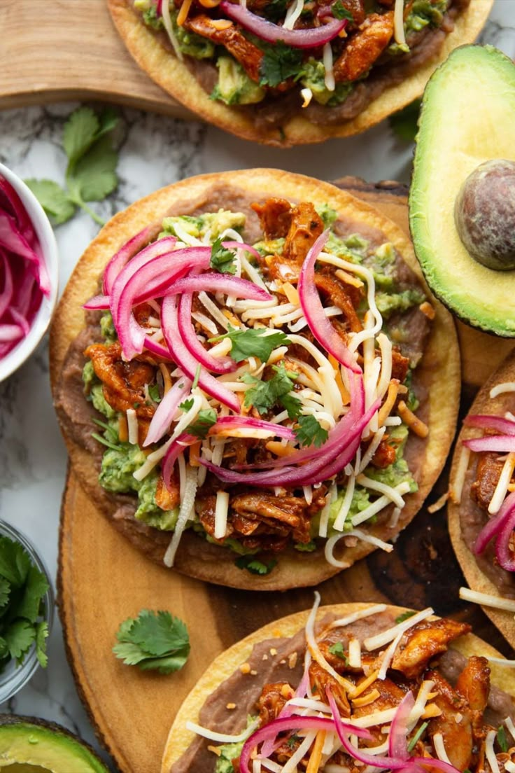 three tacos with meat, onions, lettuce and avocado on top