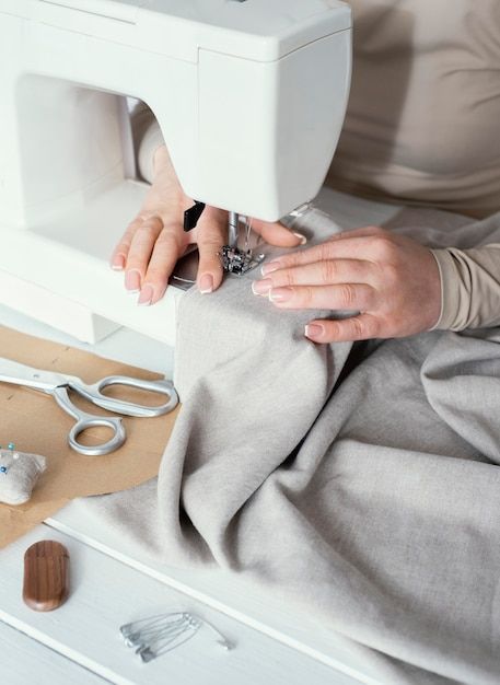 a woman is using a sewing machine to sew something on a table with scissors and other items