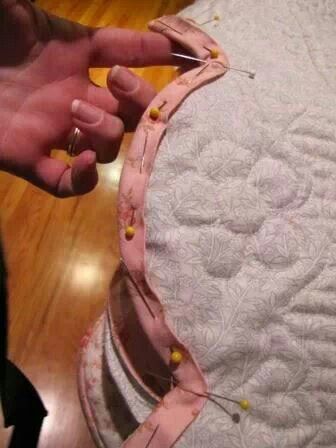 someone is sewing something on the back of a bed with pink and yellow pins sticking out of it