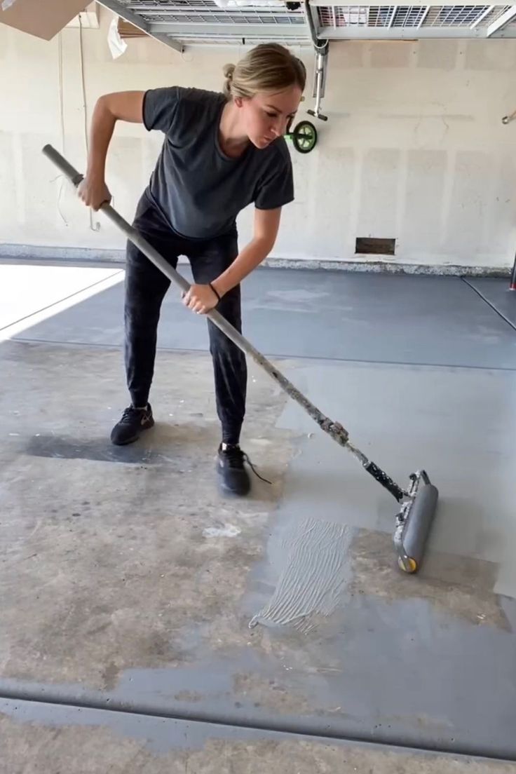 a woman with a mop is cleaning the floor in an empty garage or building