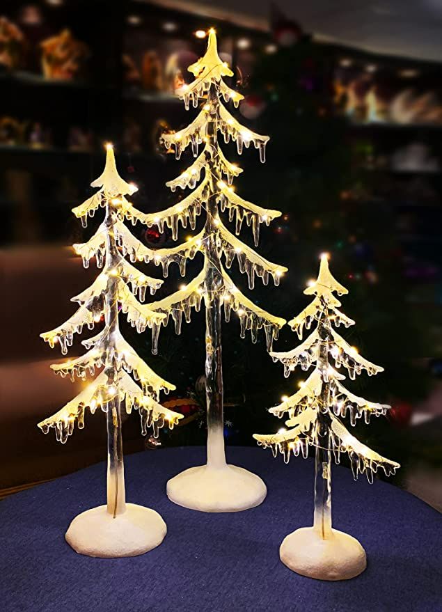 three snow covered christmas trees sitting on top of a blue table next to each other