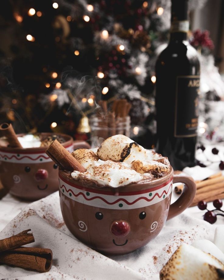 two mugs with hot chocolate and marshmallows in front of a christmas tree