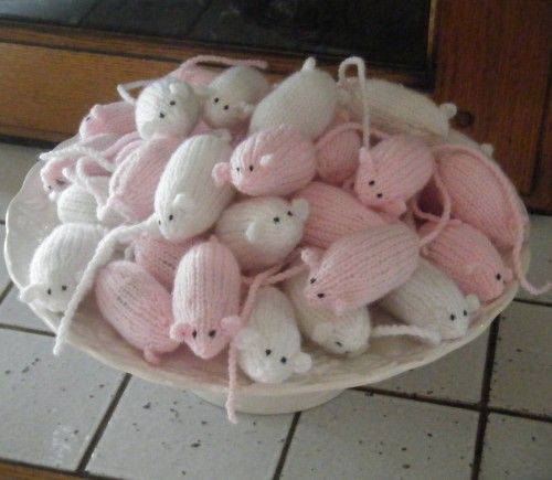 a white bowl filled with pink knitted mice on top of a tiled floor next to a door