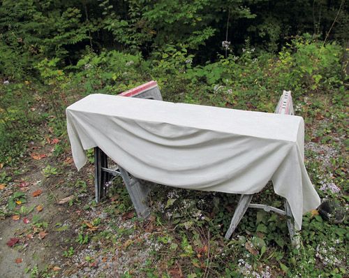 an old table covered with a sheet in the middle of a field next to some trees