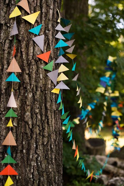 colorful paper cranes hanging from the bark of a tree in a park or forest area