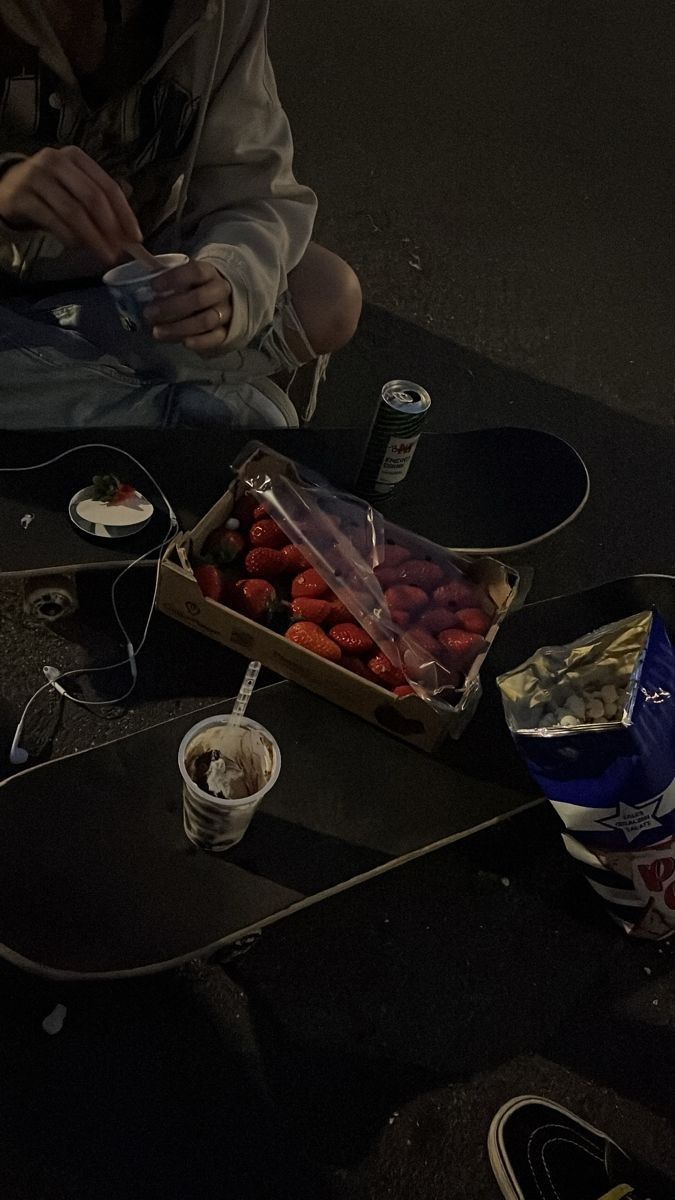 a person sitting on a skateboard next to a box of strawberries and ice cream