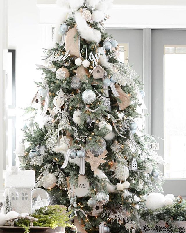 a decorated christmas tree in a living room with white and silver ornaments on the top