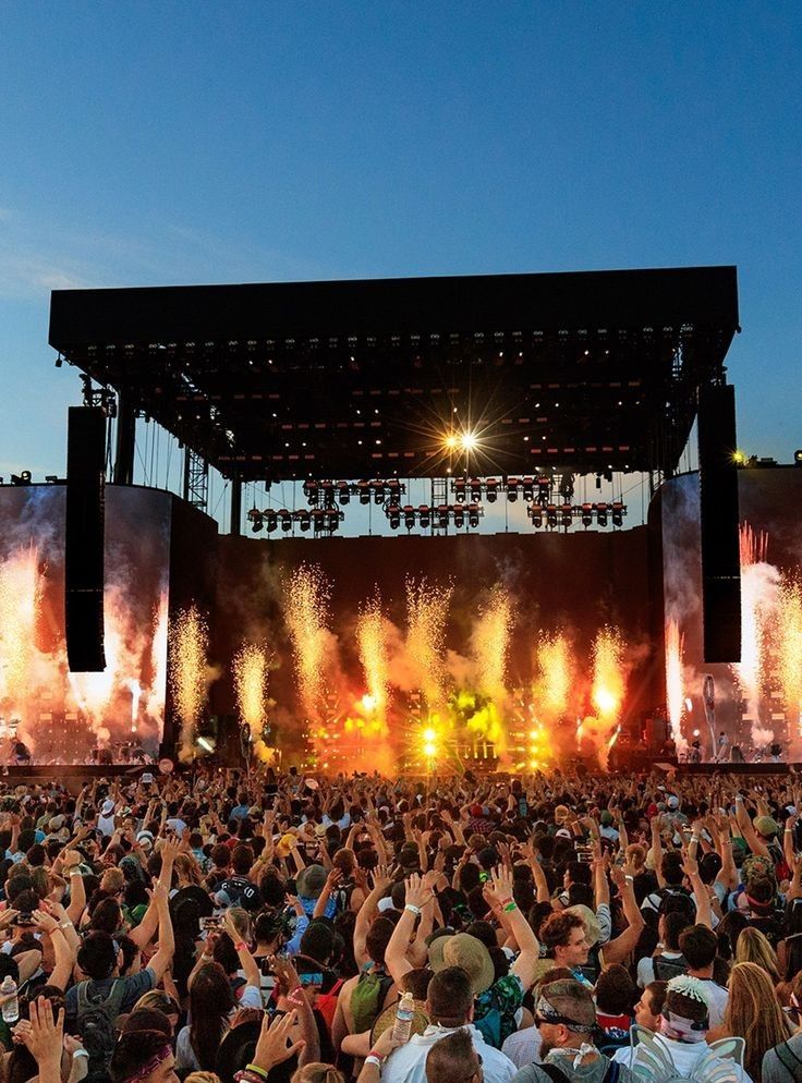 a large group of people at a concert with their hands in the air and fireworks coming out