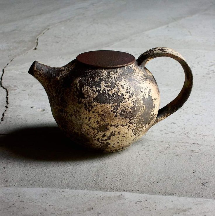 an old teapot sitting on the ground in front of a cracked concrete wall and floor