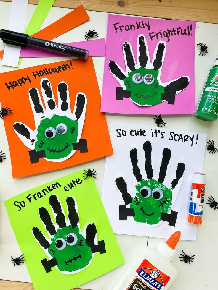 four handprinted halloween cards on a table with markers and glue, one is green and the other is orange