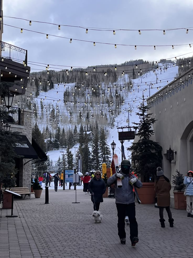 people are walking down the street in front of a ski slope with lights strung over it