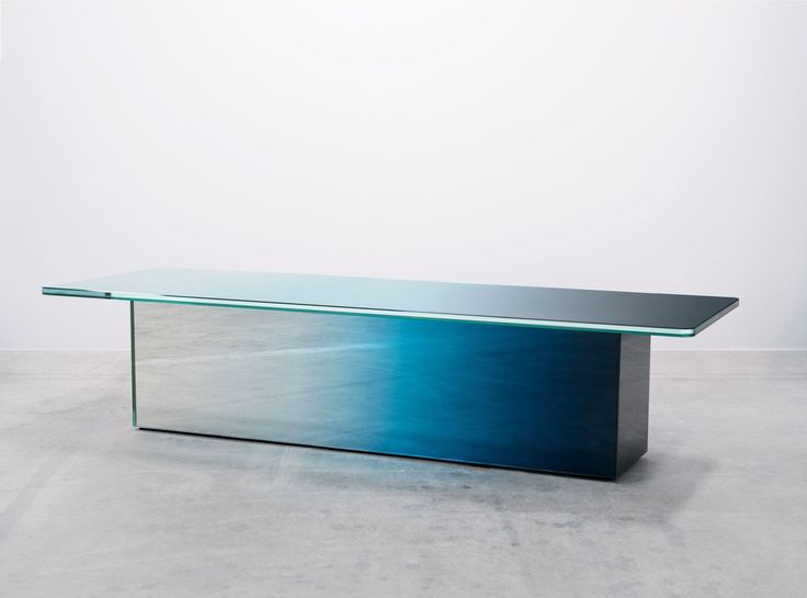 a glass table sitting on top of a cement floor next to a white wall in an empty room