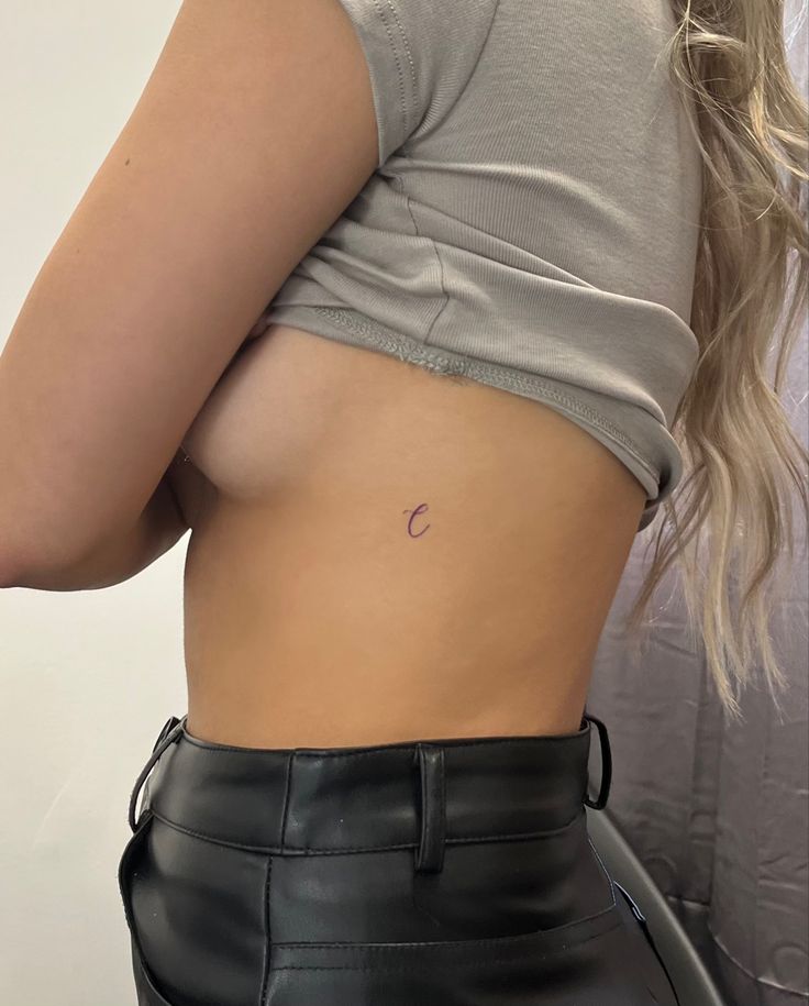 a woman's stomach with a small circle tattoo on her left side, and a black leather skirt underneath