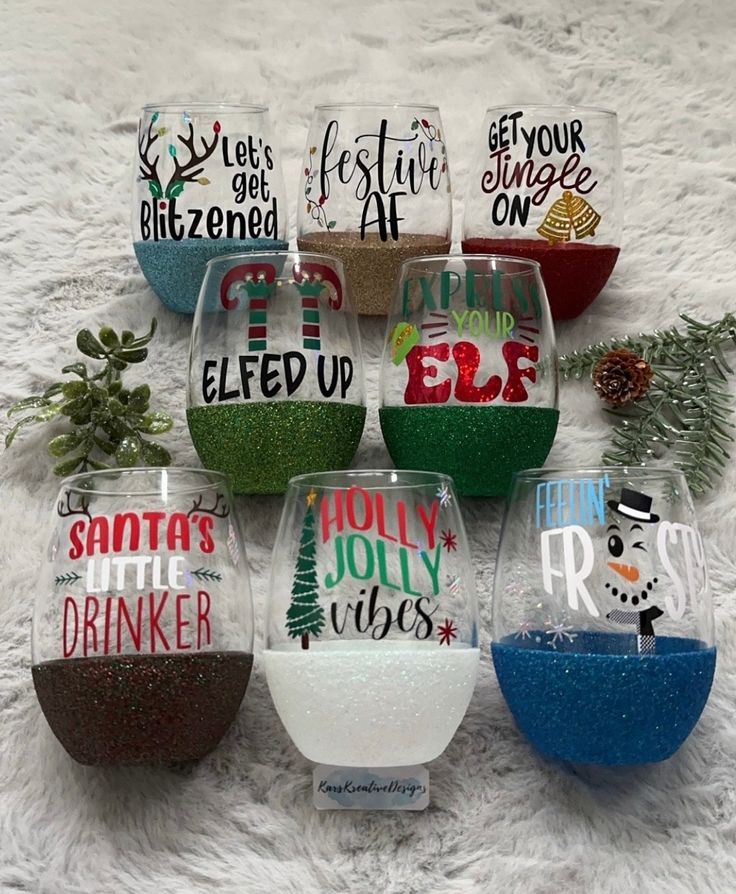 six wine glasses with different designs on them sitting on a white carpet next to pine cones