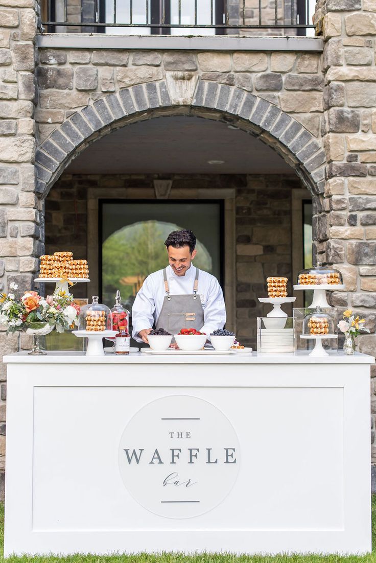 a man standing behind a counter in front of a building with cakes and pastries on it