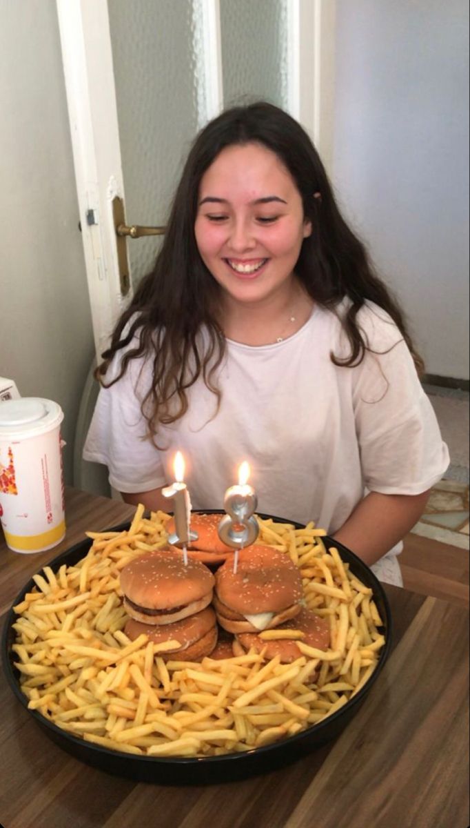 a woman sitting in front of a plate with french fries and hamburgers on it