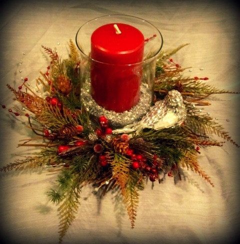 a red candle sitting on top of a glass vase filled with greenery and berries