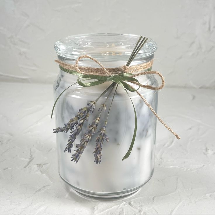 a glass jar filled with lavender flowers on top of a white tablecloth covered surface