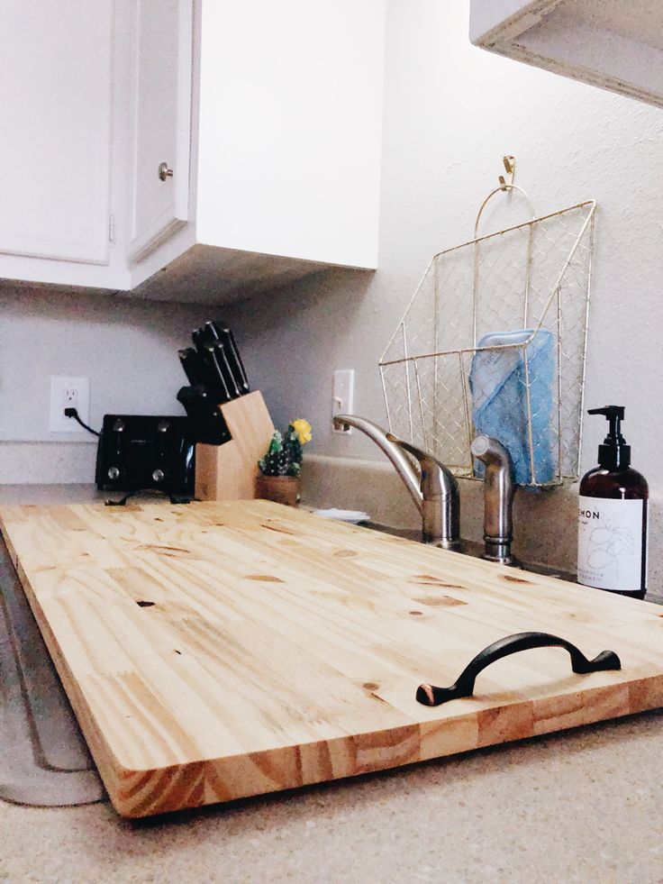 a wooden cutting board sitting on top of a kitchen counter next to a faucet