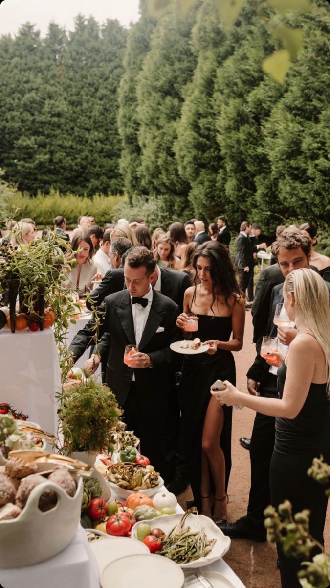 a group of people standing around a table with plates and food on top of it