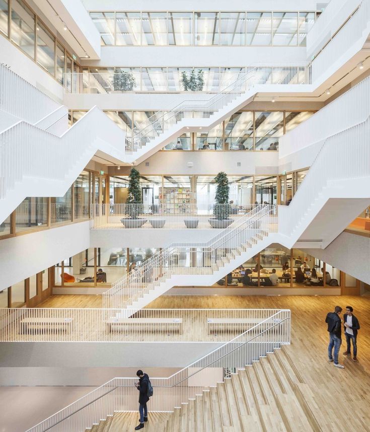 two people are walking up and down the stairs in a large building with many windows