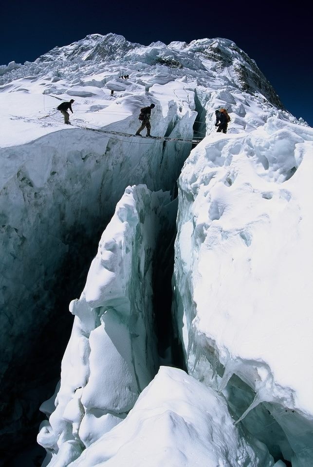 three people climbing up the side of a snow covered mountain in an ice cave,