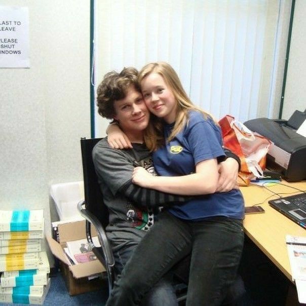 two people hugging each other in an office cubicle next to a desk with computers on it