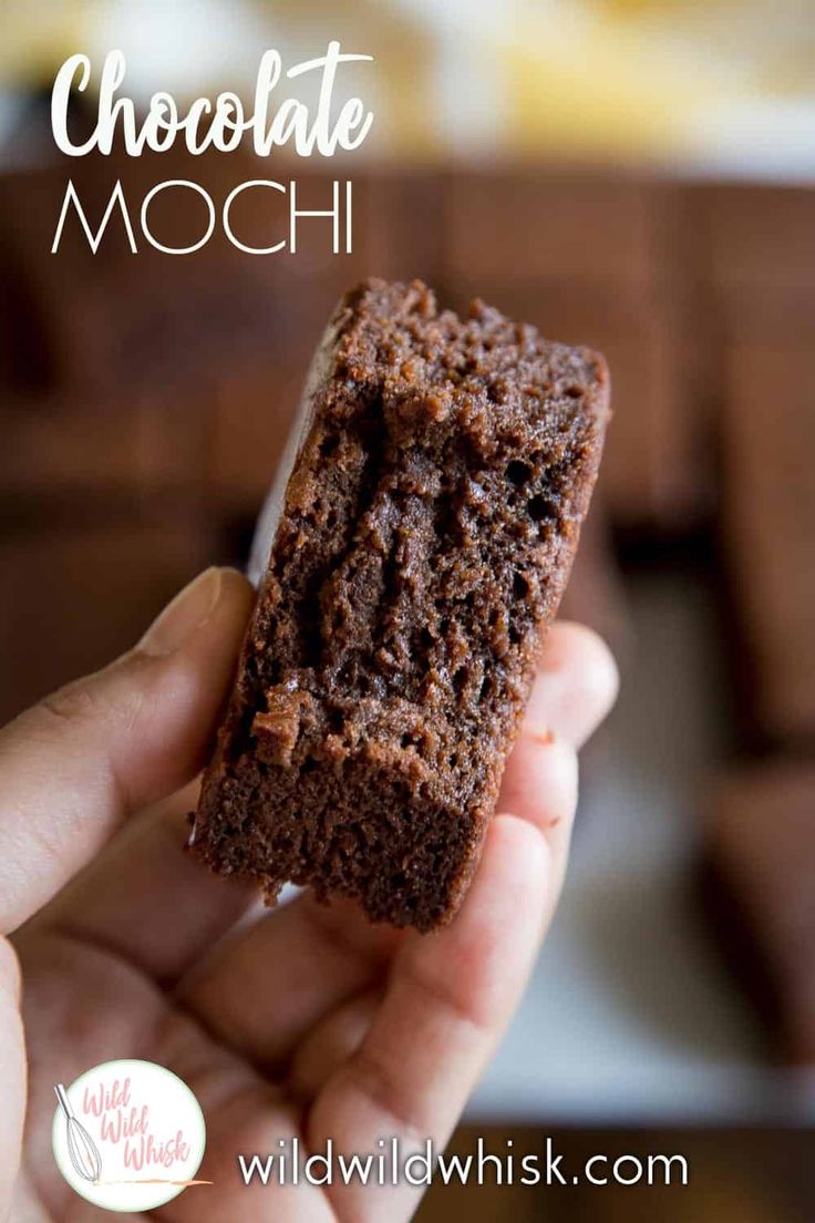 a hand holding a piece of brownie in front of a plate with chocolate squares on it