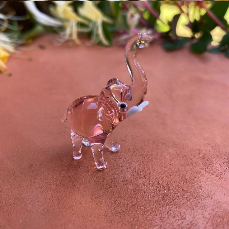 a glass elephant figurine sitting on top of a pink surface next to flowers