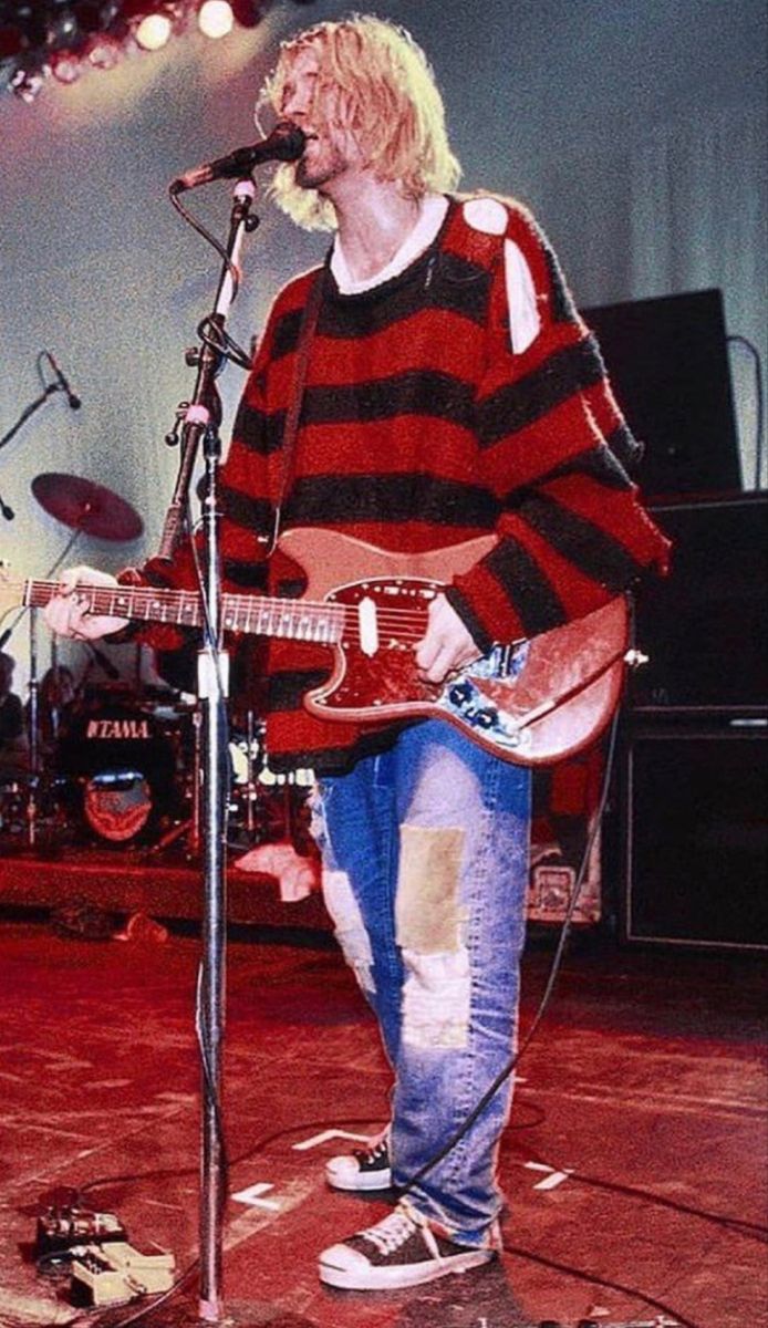 a man standing in front of a microphone while holding a guitar