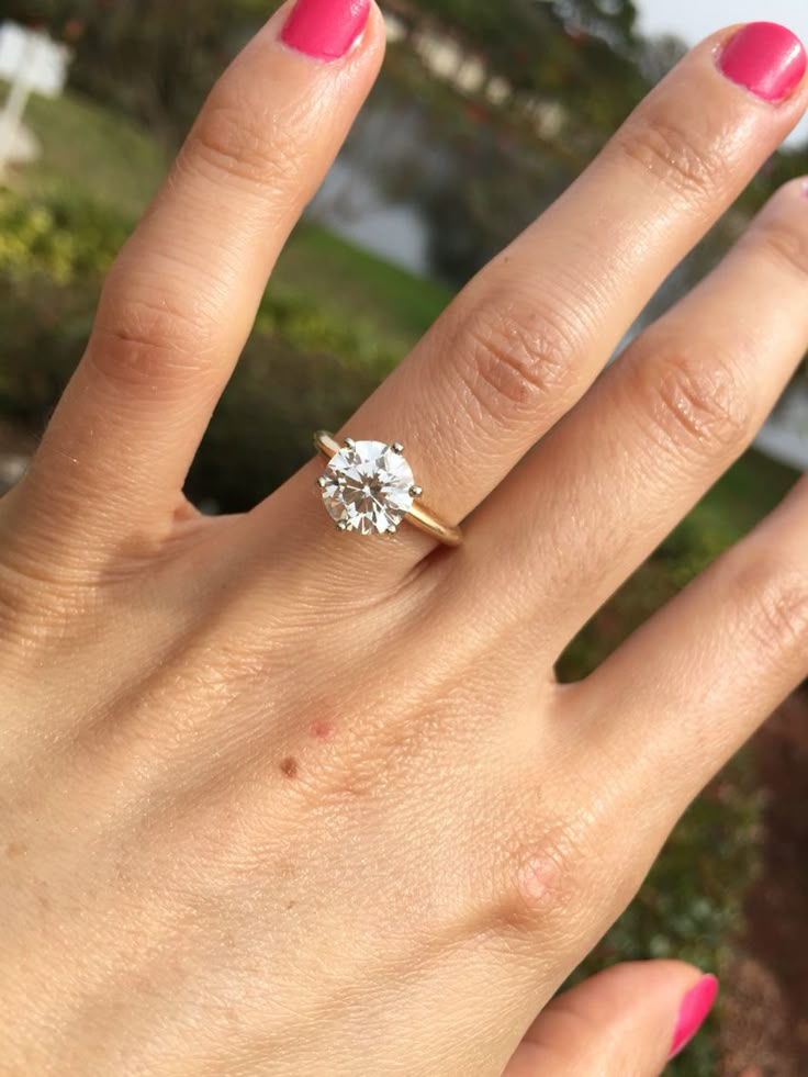 a woman's hand with a pink manicured nail polish holding a diamond ring