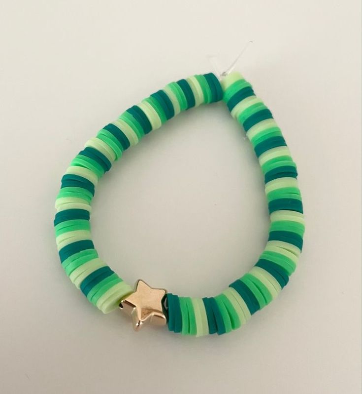 a green and white bracelet with a gold star charm on it's end, sitting against a white background