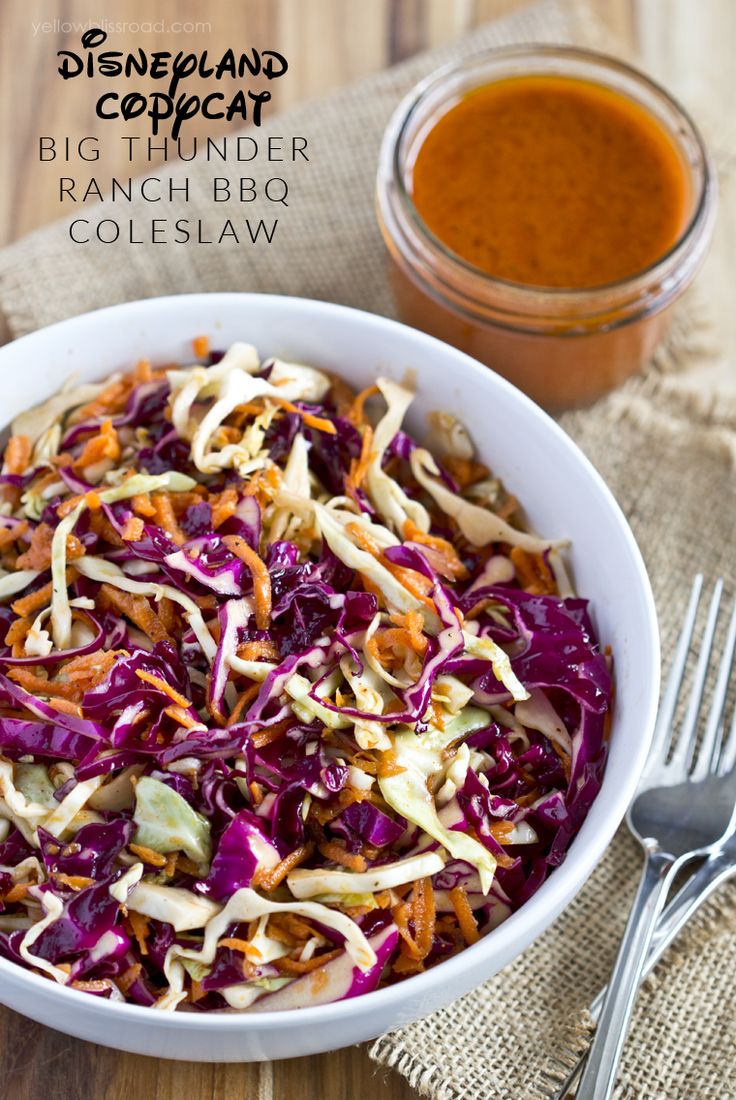 a white bowl filled with coleslaw next to a fork and spoon on top of a wooden table