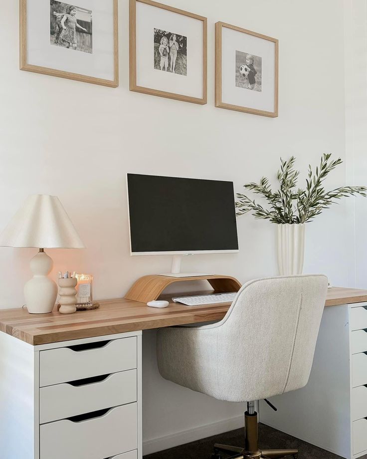 a white desk topped with a computer monitor next to a lamp and a vase filled with flowers