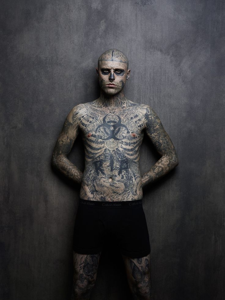 a tattooed man standing in front of a wall