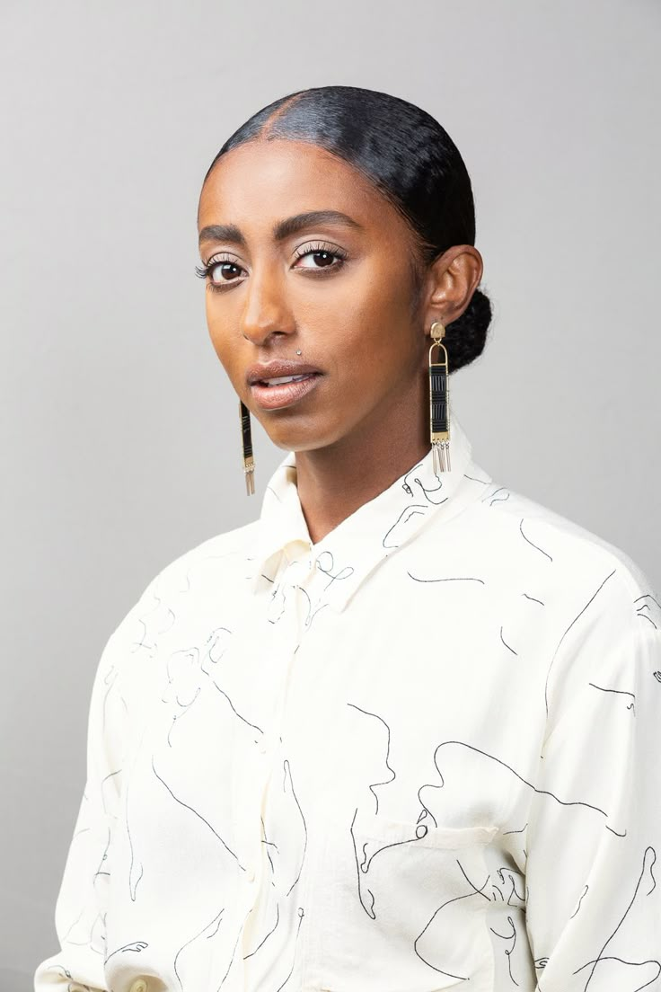 a woman with black hair wearing earrings and a white shirt