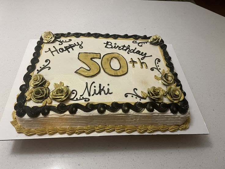 a 50th birthday cake on a table with white and black frosting, decorated with gold roses