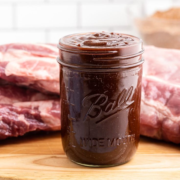 a jar filled with bbq sauce sitting on top of a wooden cutting board next to meat