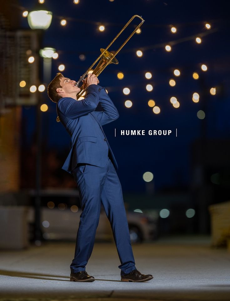 a man in a blue suit playing a trumpet on the street with lights strung overhead