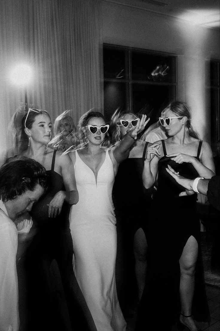 black and white photograph of women in evening dresses dancing at a party with one woman wearing sunglasses