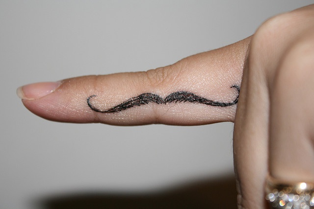 a finger with a mustache tattoo on it