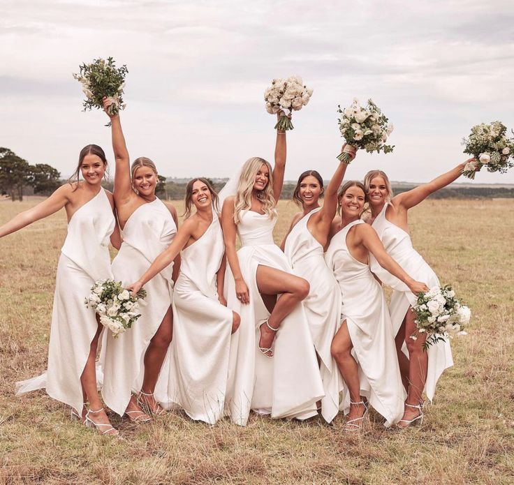 a group of women in white dresses holding bouquets and posing for a photo together